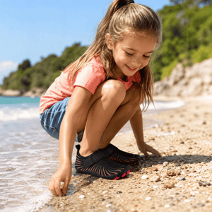 Child wearing black and pink TrailGuard Junior water shoes during outdoor play near water