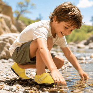 Child wearing yellow TrailGuard Junior water shoes during outdoor play near water