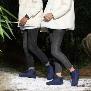 Two people wearing white puffer jackets and dark pants walking outdoors with greenery in the background.