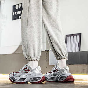 A person wearing light gray jogger sweatpants, a black t-shirt, and chunky white and red sneakers, standing in an indoor setting.