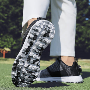 A close-up lifestyle shot of a person's legs on a golf course, showing the sole of a black and white golf shoe with black spikes, paired with white pants.