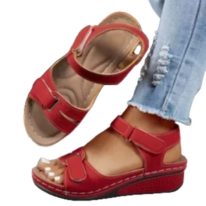 Red peep-toe wedge sandals with double straps, shown on a model wearing light blue distressed jeans against a white background.