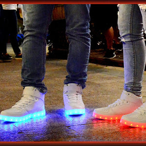 Two people standing outdoors at night wearing white high-top sneakers with glowing LED soles, one emitting blue light and the other emitting red light.