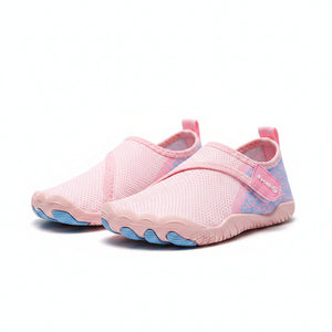 A close-up of a person's legs standing on sandy ground wearing pink and light blue toeless water shoes.