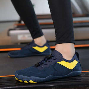 A close-up of a person wearing dark navy blue minimalist sneakers with bright yellow accents, standing on a treadmill in a gym.