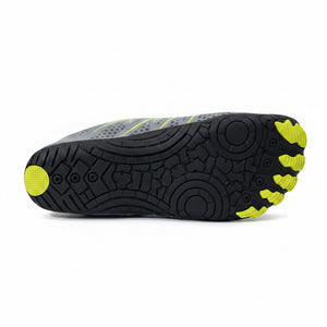 The sole of a gray and black minimalist shoe with bright yellow accents, photographed on a light gray tiled floor.