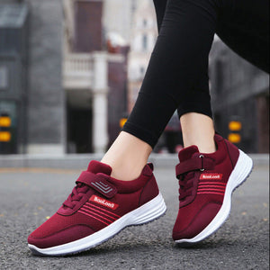 A pair of women's low-top athletic sneakers in burgundy red and white, featuring hook-and-loop strap closures and a visible 'SooLong' brand logo. The top half shows the shoes being worn by a person in an outdoor urban setting, while the bottom half shows a clean close-up of the shoes on a paved surface.