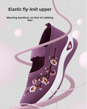 A purple knit slip-on shoe with floral embroidery on the side, shown against a light gray background with decorative pink ribbon swirls and text describing the elastic fly-knit upper.