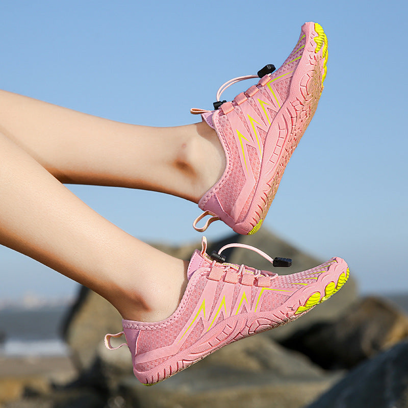 Pink water shoes with yellow accents worn by a person on a beach.