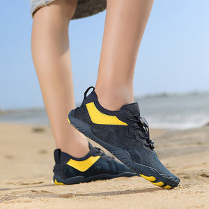 A person wearing black and yellow athletic sneakers walking on a sandy beach with the ocean in the background.