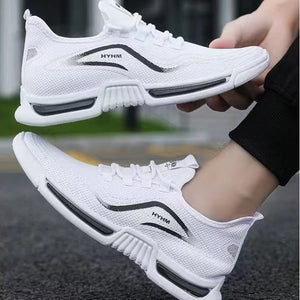 White athletic sneakers with black accents, shown being worn and held by a person outdoors on a paved surface.