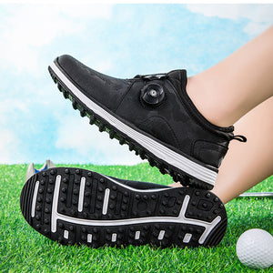 Black low-top golf shoes with a dial closure and white midsoles, shown on a person's foot and sole against a grassy golf course background with a golf ball.