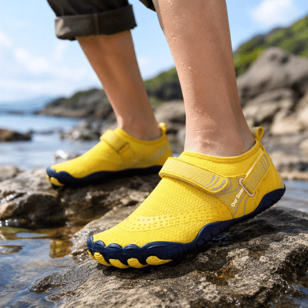 Adult wearing yellow TrailGuard wide-toe water shoes near a rocky shoreline