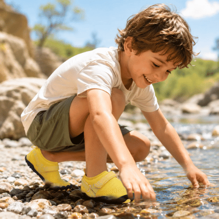 Child wearing yellow TrailGuard Junior water shoes during outdoor play near water