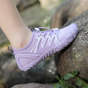 A close-up of a person's foot wearing a light purple athletic shoe with white accents, resting on a large rock in an outdoor setting.