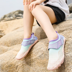 A child model sitting on rocks outdoors wearing pastel gradient athletic shoes, a white T-shirt, black shorts, and a green cap, with promotional text on the left side.