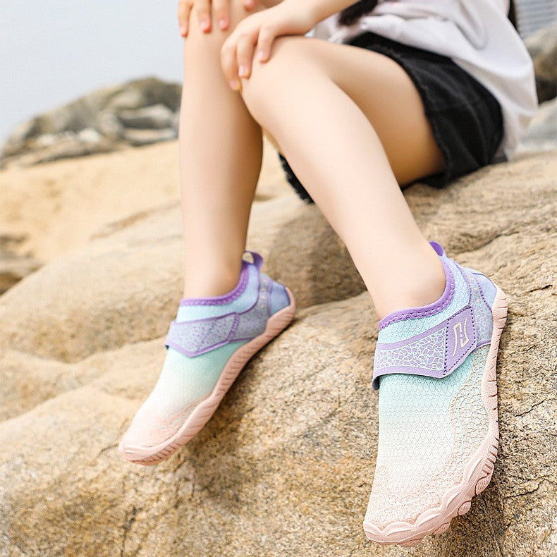 A child model sitting on rocks outdoors wearing pastel gradient athletic shoes, a white T-shirt, black shorts, and a green cap, with promotional text on the left side.
