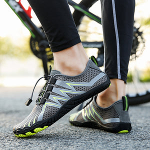 Gray water shoes with neon green and silver accents, worn by a person standing on pavement with a bicycle blurred in the background.
