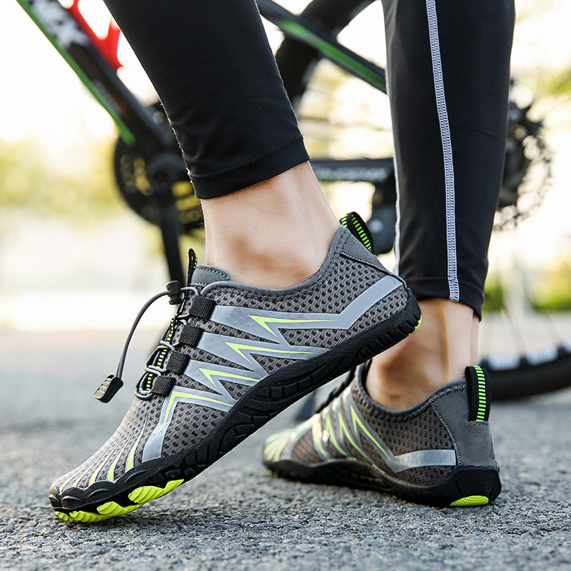 Gray water shoes with neon green and silver accents, worn by a person standing on pavement with a bicycle blurred in the background.
