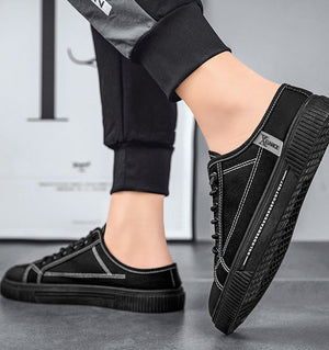 Black sneakers worn with black pants on a gray floor.