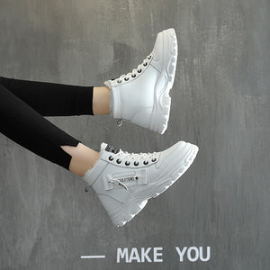 White high-top sneakers worn by a person against a gray background