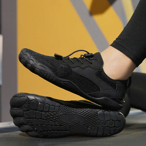 Black minimalist running shoes with a breathable mesh upper and flexible sole, shown on a treadmill with one shoe lifted by a person's foot.