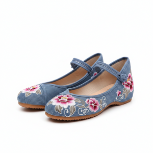 A pair of blue suede flat shoes with pink and white floral embroidery on the toe, displayed on a clean white background.