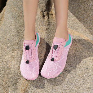 Pink mesh athletic shoes with turquoise accents and black toggle laces, shown on a person standing on a rocky outdoor surface.