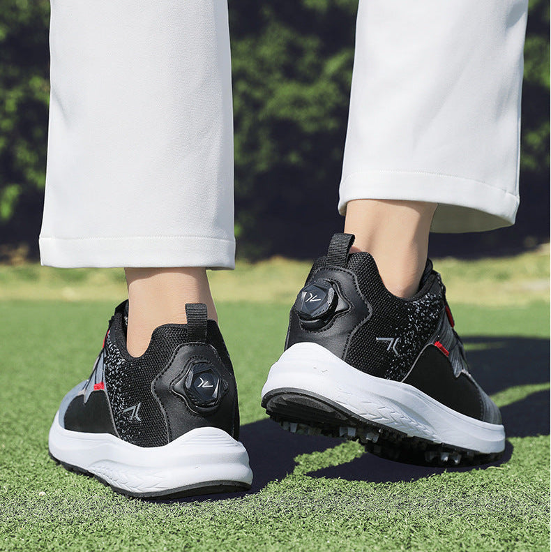 A pair of athletic sneakers shown on a person outdoors on grass, with the lower legs and feet visible. The shoes are primarily black and gray with white midsoles and small red accents.