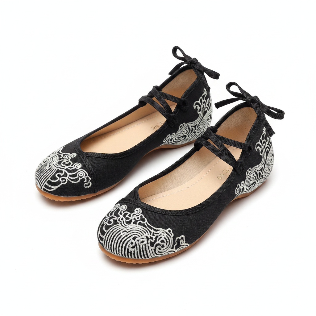 A pair of black flat shoes with traditional Chinese wave embroidery in white and black, featuring lace-up straps and bow details on the back, shown on a white background.
