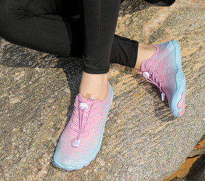 A person wearing pink and light blue gradient athletic sneakers while sitting on a textured stone surface outdoors.
