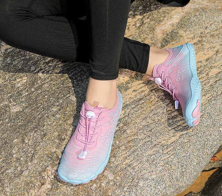 A person wearing pink and light blue gradient athletic sneakers while sitting on a textured stone surface outdoors.