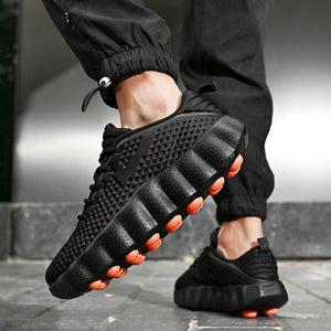 Black casual shoes with orange accents worn by a person in black pants.