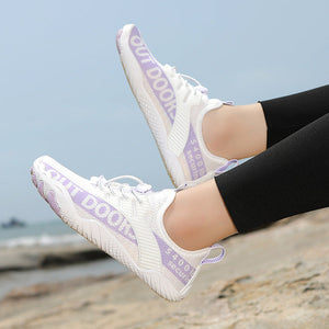 White sneakers with purple text worn by a person on a beach.