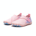 A close-up of a person's legs standing on sandy ground wearing pink and light blue toeless water shoes.