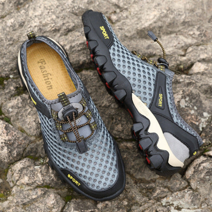 A pair of gray and black mesh athletic water shoes with gold laces and yellow accents, shown in two views on a rocky outdoor background.