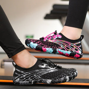 A pair of women's water shoes shown on a treadmill, with one shoe worn on a foot and the other floating above the treadmill belt. The shoes feature a black mesh upper with pink, blue, and white graphic accents.