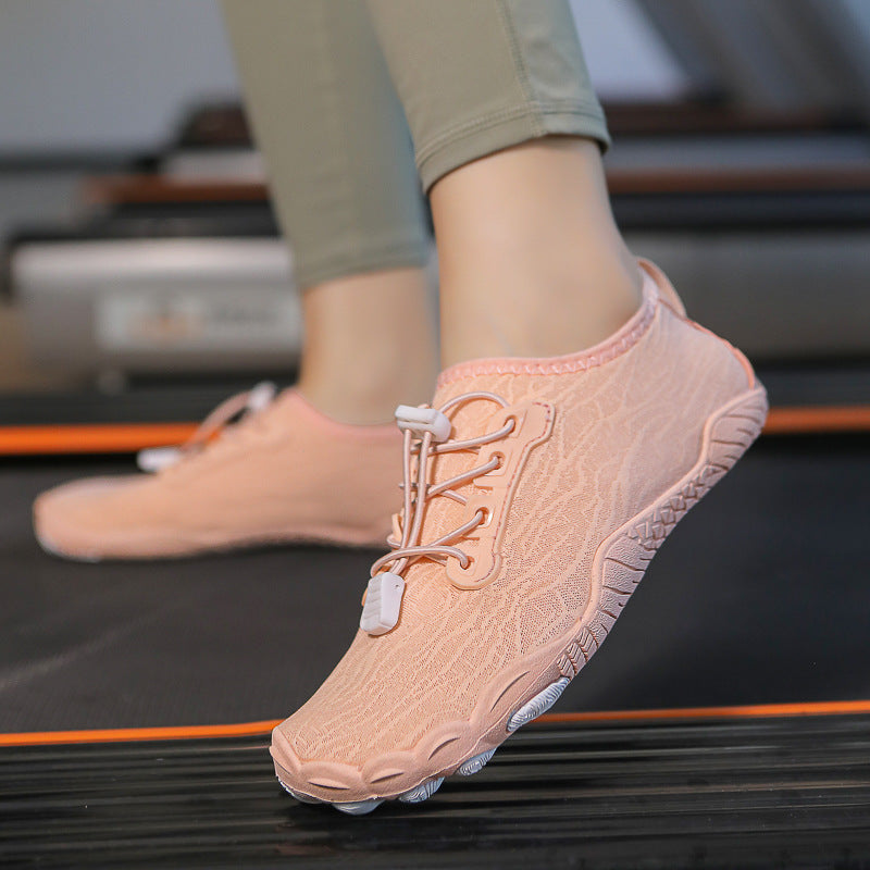 A close-up of a person wearing a light pink knit athletic sneaker while stepping onto a treadmill. The shoe has a textured knit upper, matching laces, and a flexible sole, with the person's legs in olive green leggings visible above the shoe.