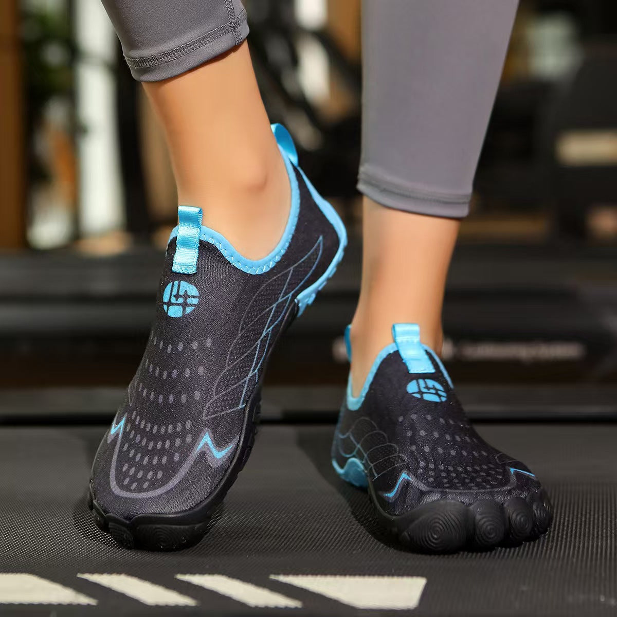 A person wearing gray leggings and black water shoes with bright blue accents, standing on a treadmill in a gym setting.