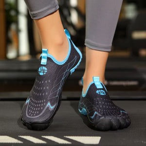 A person wearing gray leggings and black water shoes with bright blue accents, standing on a treadmill in a gym setting.