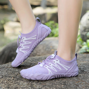 A pair of light purple athletic sneakers with white accents, shown on a person's feet standing on a stone outdoors.