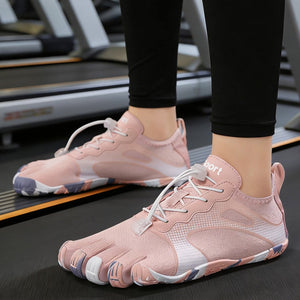 A close-up of a person's feet wearing light pink minimalist toe-fit running shoes with white laces, standing on a gym treadmill.