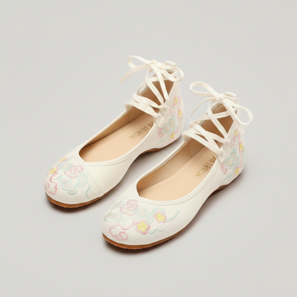 A pair of white flat shoes with delicate lace-up front straps and pastel embroidered floral details on the toe, photographed on a light gray background.