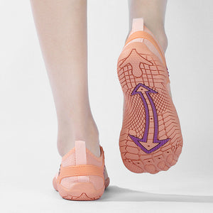 A pair of peach-colored water shoes being worn, with one shoe shown from the back to display the textured sole featuring a purple anchor graphic.