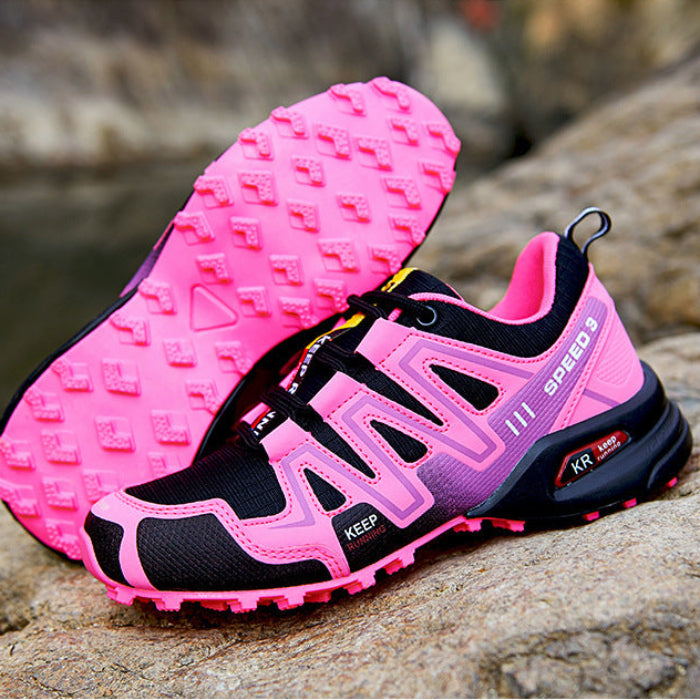 Pink and black athletic shoes with textured soles on a rock surface