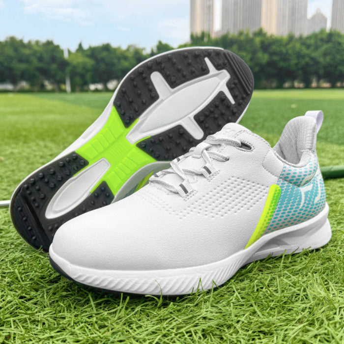 A pair of white athletic sneakers with bright green and blue accents, shown on a grassy field with trees and buildings in the background. One shoe is standing upright while the other lies on its side to show the sole.