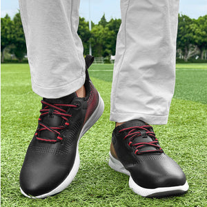 A person wearing black athletic sneakers with red laces and white soles, standing on green grass outdoors.
