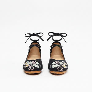 A pair of black flat shoes with lace-up ankle straps and embroidered floral details on the toe, shown from the back against a plain white background.