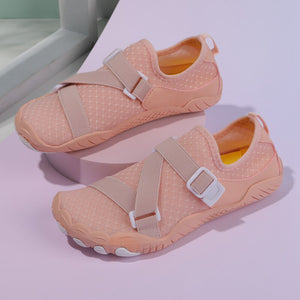 A pair of peach-colored water shoes with beige adjustable straps and white buckles, displayed on a light purple surface.