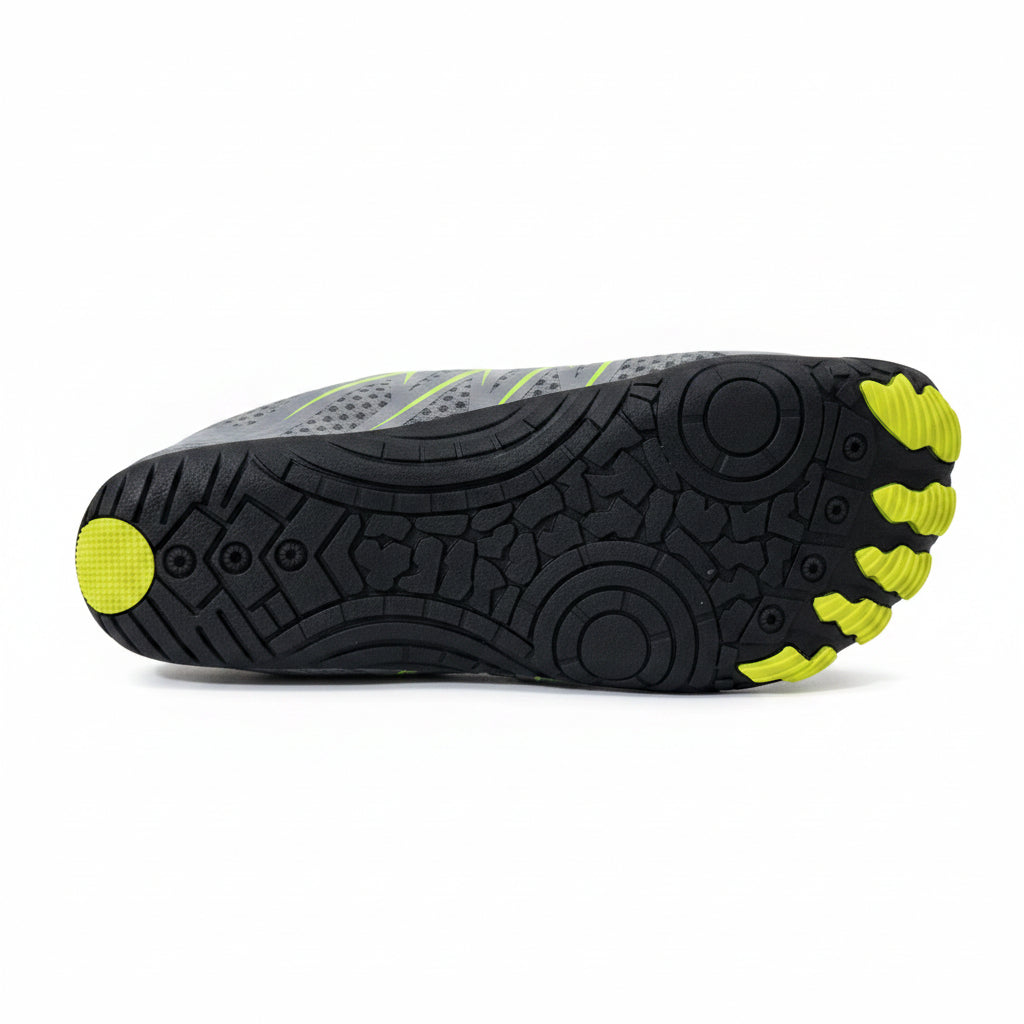 The sole of a gray and black minimalist shoe with bright yellow accents, photographed on a light gray tiled floor.